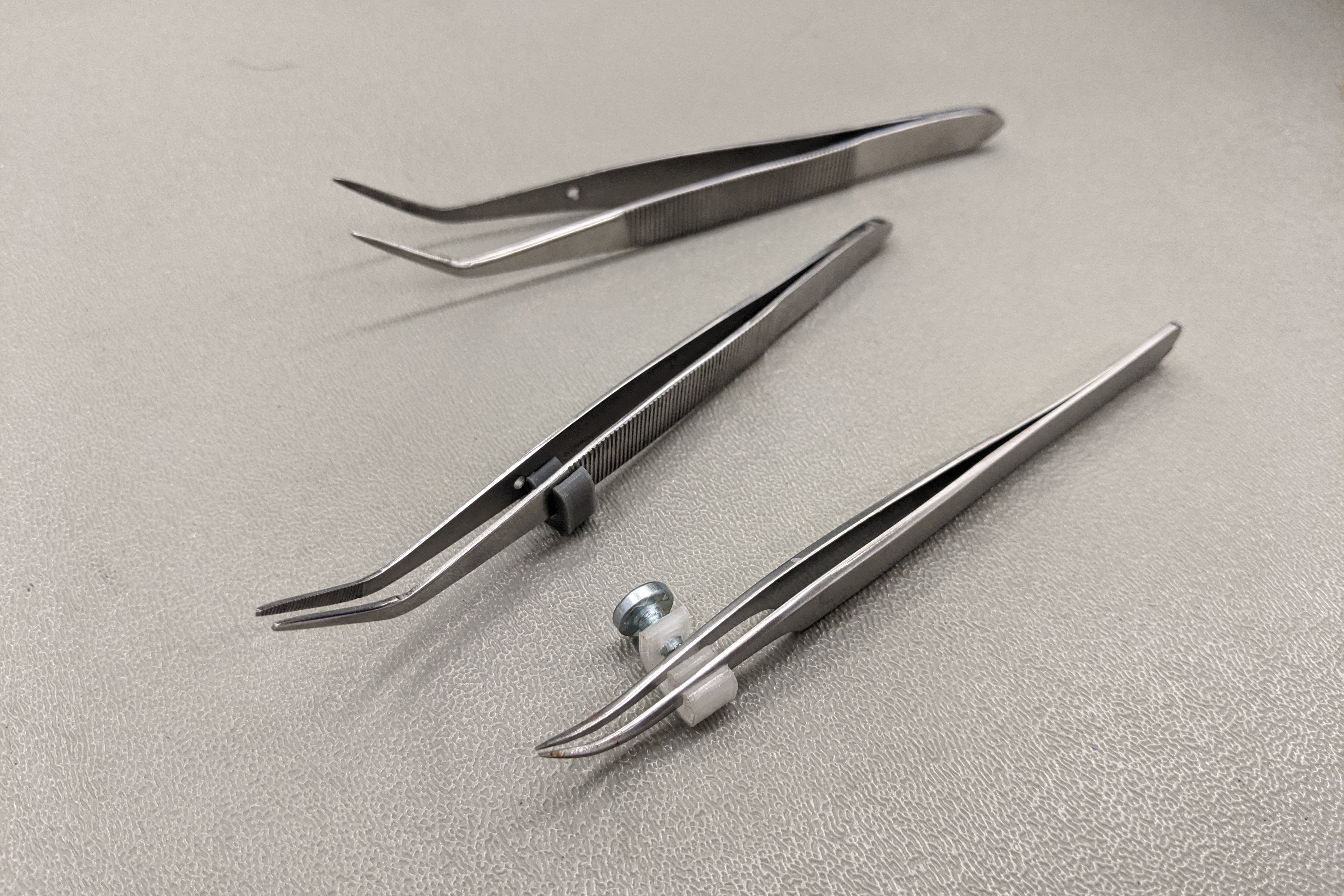 An adjustable attachment which limits a tweezer's range of movement and allows for finer control